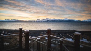 A view of a mountainous landscape with a body of water and a stone staircase leading down to the shore. - Glacier + Tide Residence (Homer)