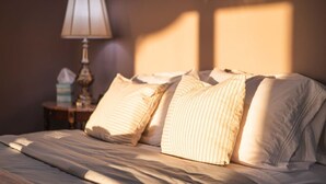 A bed with striped pillows and a lamp on a bedside table. - Little Glacier + Tide (Homer)