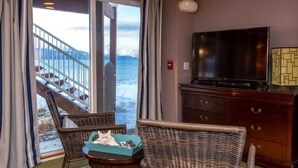 A hotel room with a balcony, a television, wicker furniture, and a view of the beach. - Little Glacier + Tide (Homer)