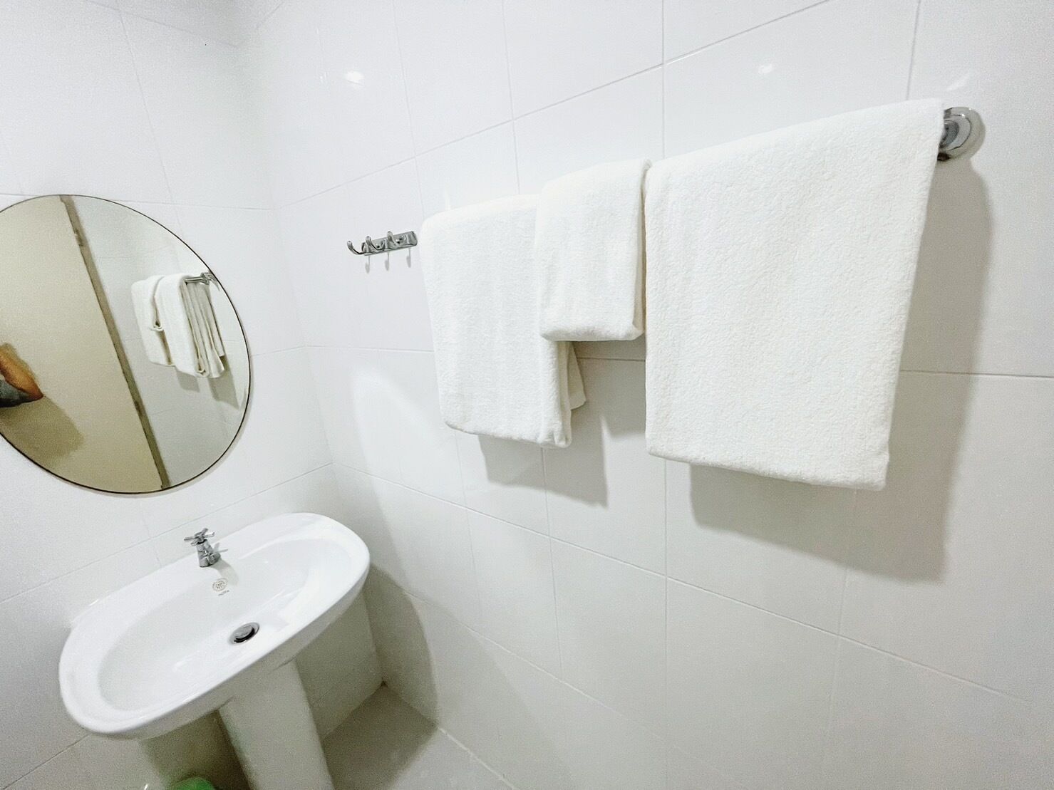A bathroom with a white sink, a round mirror, and two white towels hanging on a towel rack.