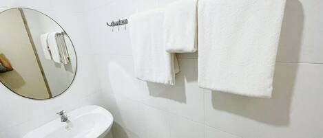 A bathroom with a white sink, a round mirror, and two white towels hanging on a towel rack.
