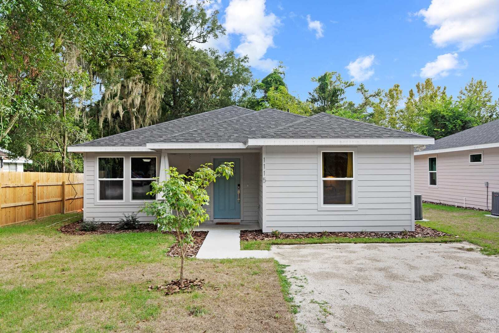 A single-story house with a gray exterior, a front porch, and a small tree in the front yard.