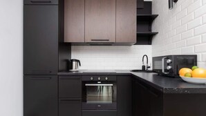 Een moderne keuken met zwarte kasten, een inbouwoven, een waterkoker en een magnetron.