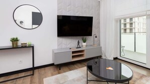 Een moderne woonkamer met een flatscreen televisie aan een gestructureerde muur, een ronde spiegel, een grijze console met decoratieve objecten, en een glazen salontafel.