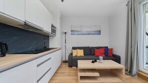 Un espacio habitable compacto con kitchenette, un sofá con cojines, una mesa de centro y un cuadro en la pared.