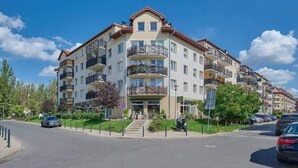 Un edificio residencial de varios pisos con balcones, una entrada central y un estacionamiento.