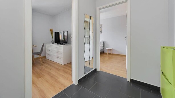 Habitación moderna y minimalista con suelo de madera, paredes blancas, una silla gris, un aparador blanco y un armario verde.