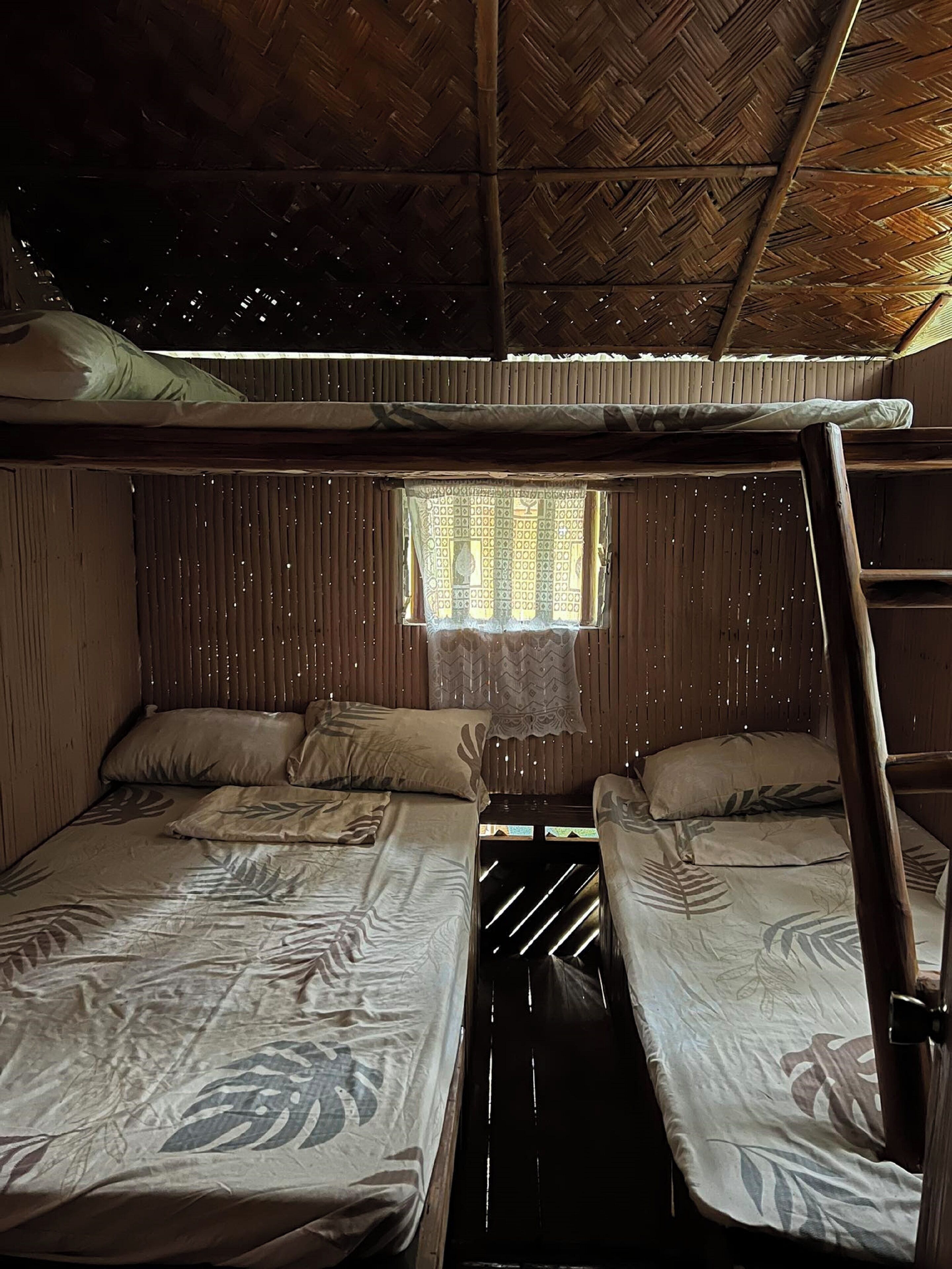 A rustic room with two bunk beds, a window with a patterned curtain, and a wooden ceiling.
