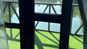 A view through a window with a metal frame, a grassy area, and a body of water with a wooden structure in the background. - Isla Del Antoño (Cavinti)