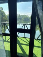 A view through a window with a metal frame, a grassy area, and a body of water with a wooden structure in the background.