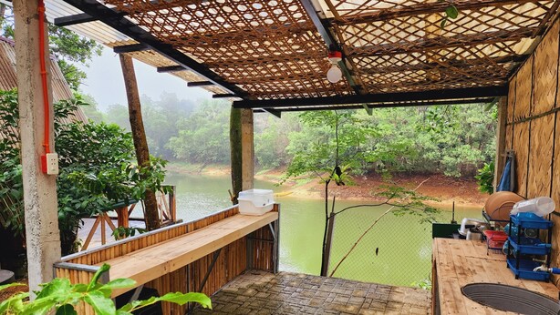A rustic wooden structure with a view of a river, a wooden bench, and a table with kitchenware. - Isla Del Antoño (Cavinti)