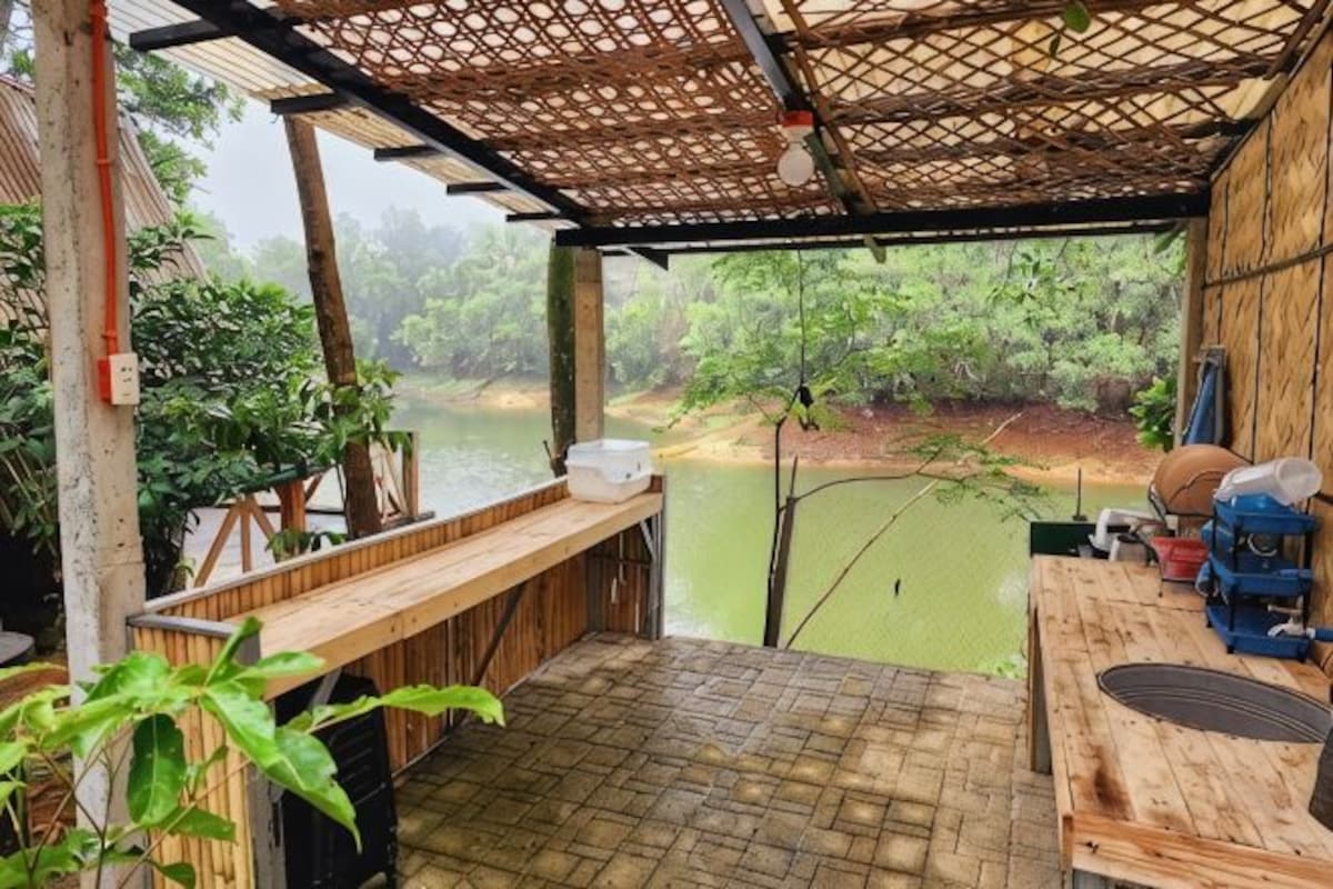 A covered outdoor area with a wooden bench, a table, and a view of a river.
