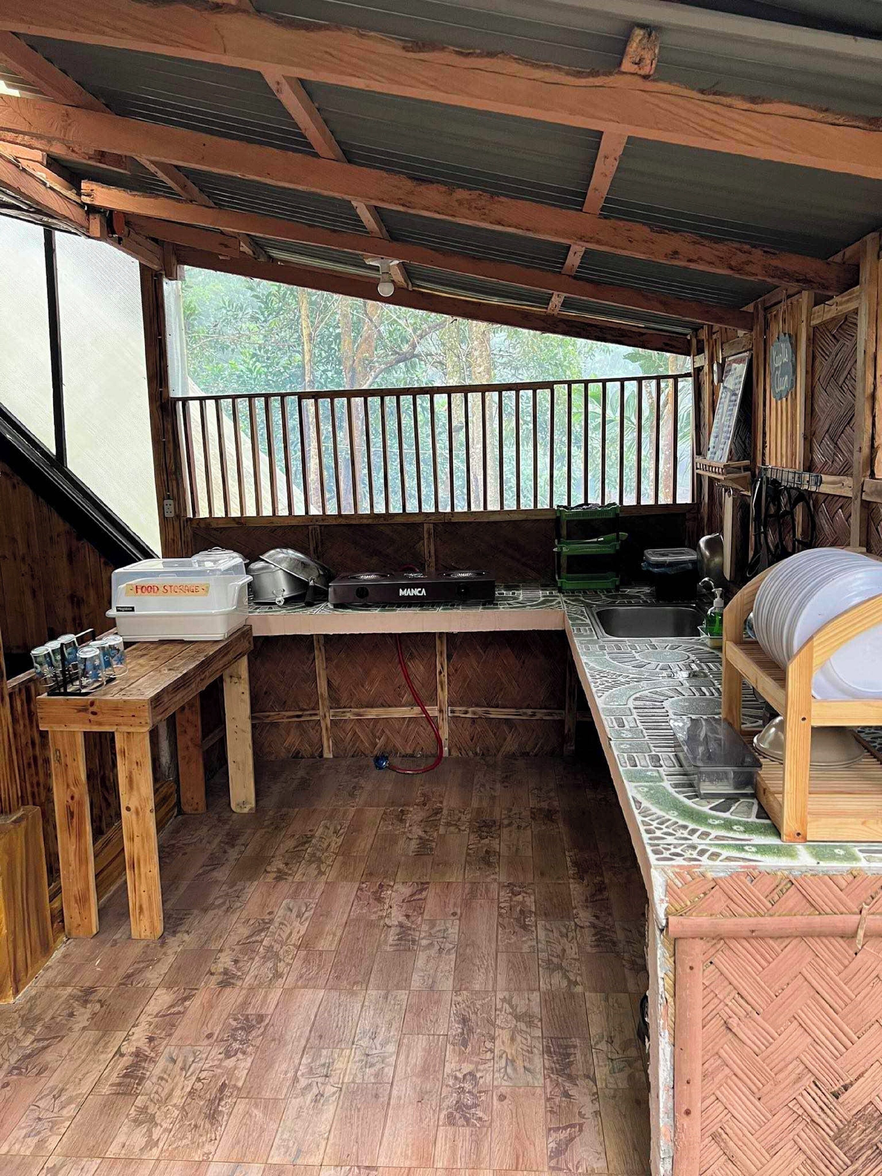 A rustic kitchen with a wooden table, a food storage unit, a stove, and a sink.