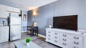 A modern kitchen with a refrigerator, stove, and microwave. There is a dining table with a plant, a TV on a white dresser, and a wall-mounted light. - Oceanfront Efficiency T507 (Myrtle Beach)