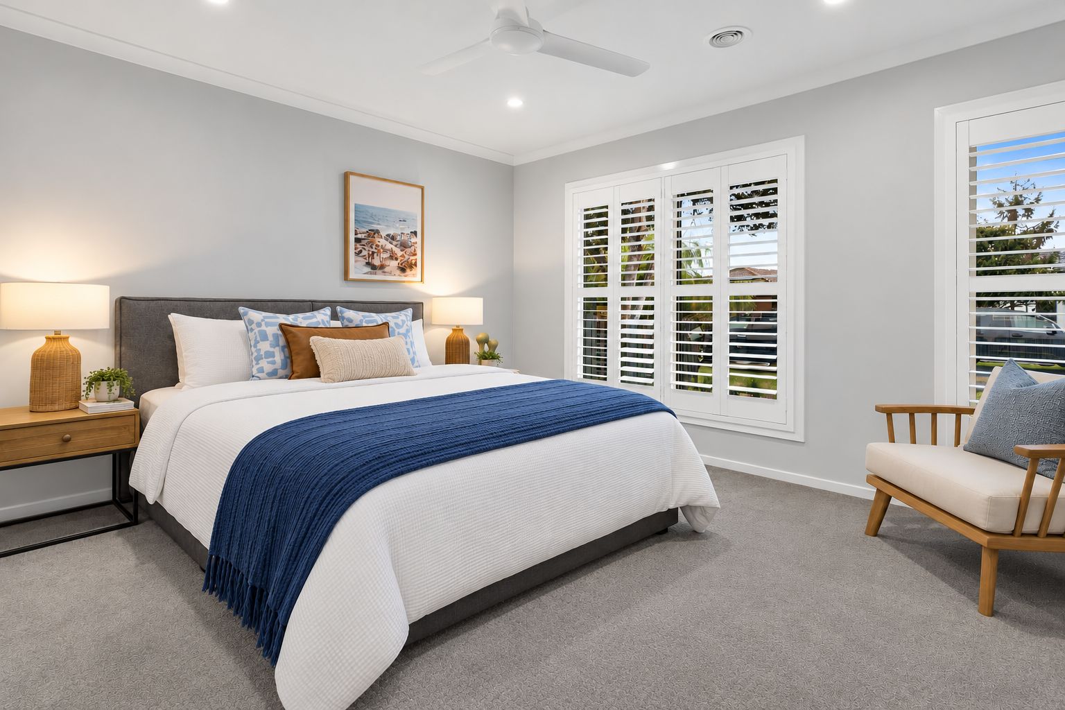 A bedroom with a bed, bedside tables, a chair, a ceiling fan, and a window with shutters.