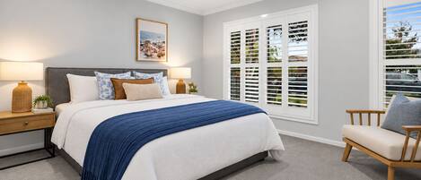 A bedroom with a bed, bedside tables, a chair, a ceiling fan, and a window with shutters.
