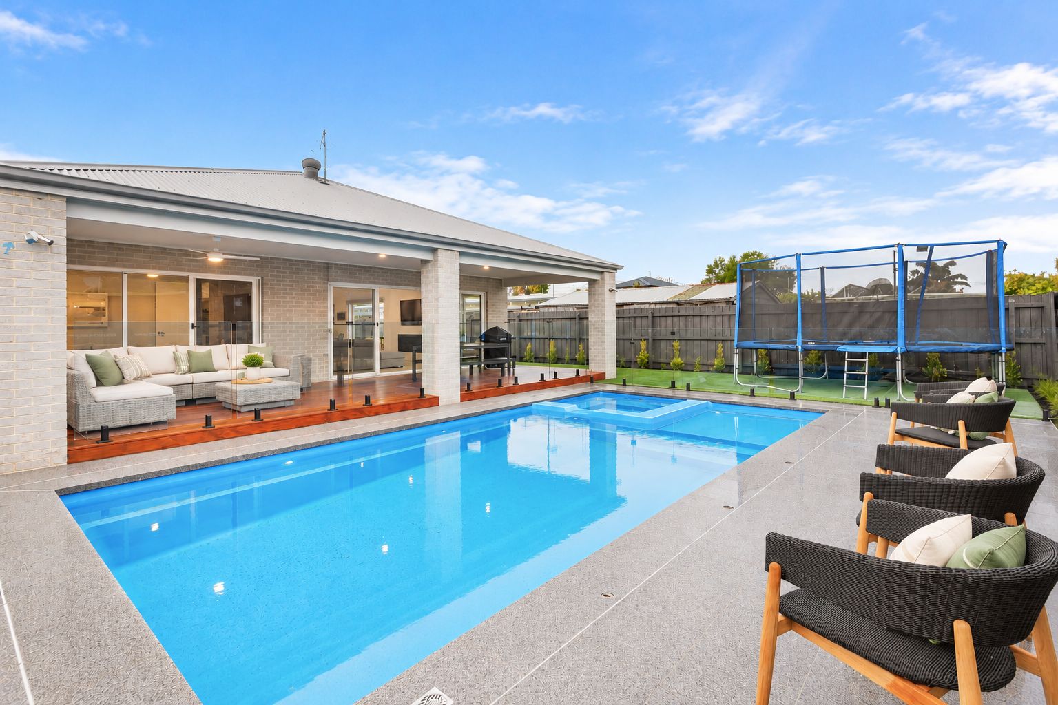 A swimming pool with a covered patio area, outdoor furniture, and a fenced play area.