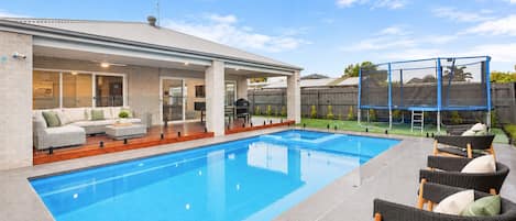A swimming pool with a covered patio area, outdoor furniture, and a fenced play area.