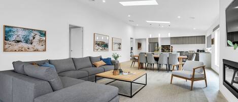 A modern living room with a sectional sofa, a coffee table, and a dining area with a kitchen in the background.