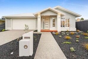 A modern single-story house with a garage, a front porch, and a landscaped garden with various plants and a gravel pathway.