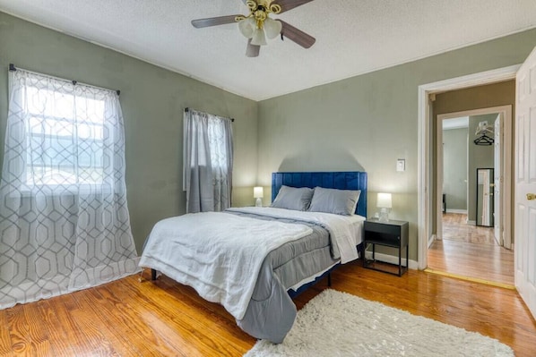 A bedroom with a bed, nightstands, a ceiling fan, and a view of a hallway.