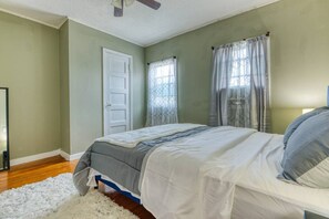 A bedroom with a bed, a door, and windows with curtains.