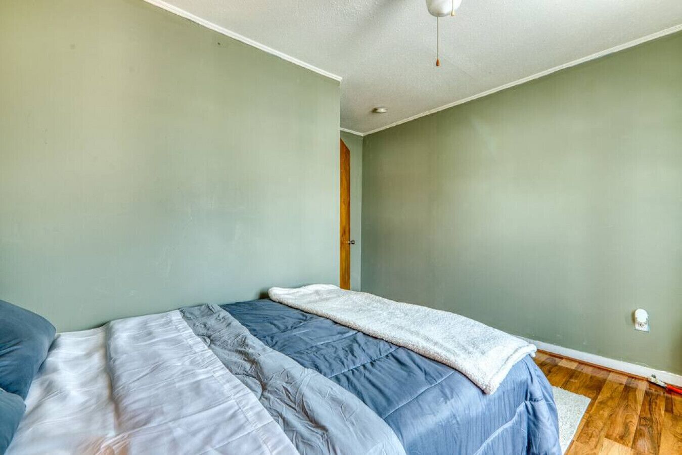 A bedroom with a single bed, a door, and a light switch on the wall.