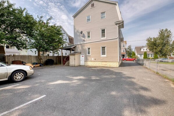 A residential area with a two-story house, a fenced yard, and parked cars.