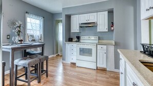 A kitchen with white cabinets, a stove, and a dining area with a table and chairs.
