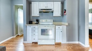 A compact kitchen with white cabinets, a stove, and a coffee maker.
