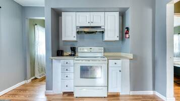 A compact kitchen with white cabinets, a stove, and a coffee maker.