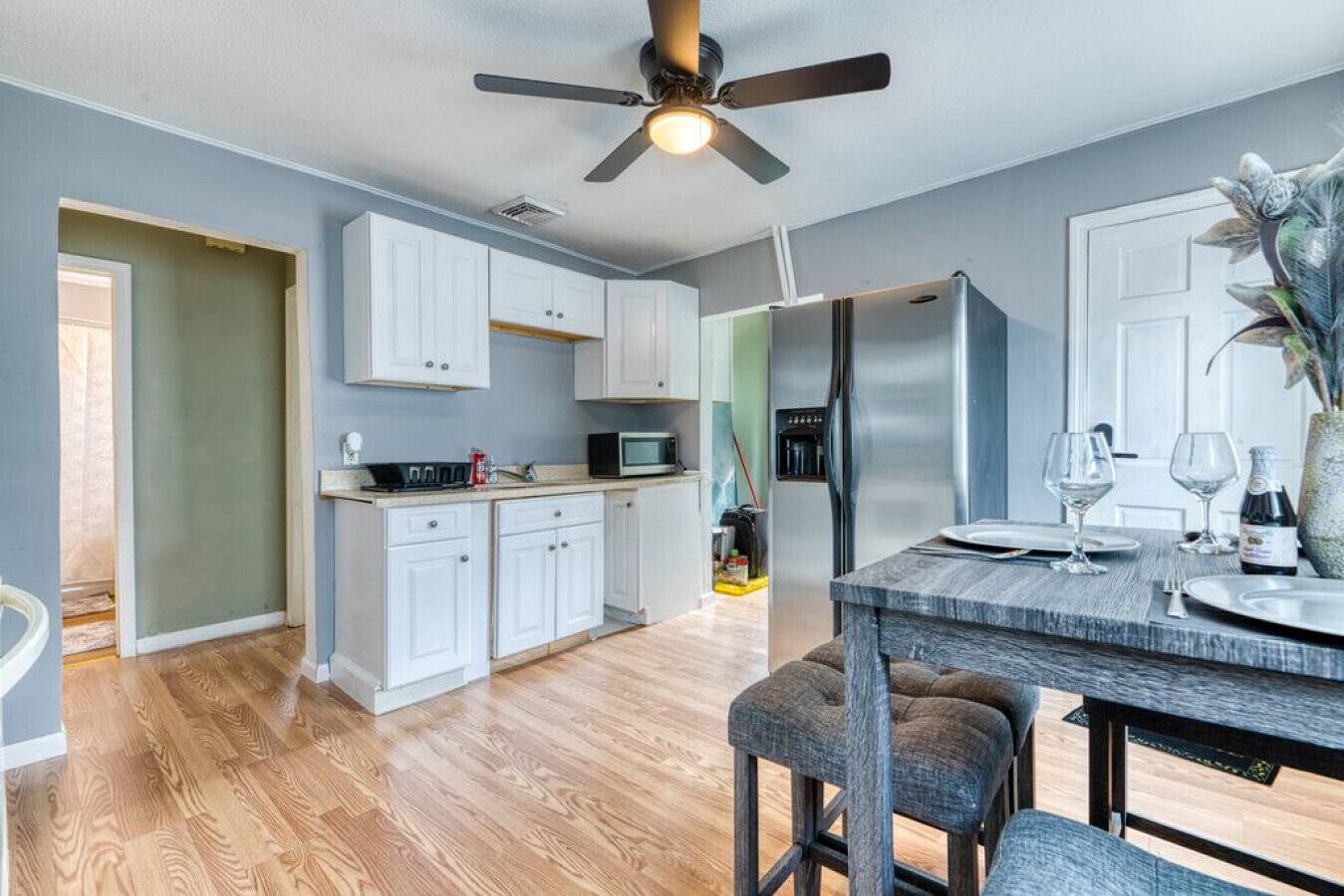 A modern kitchen with white cabinets, a stainless steel refrigerator, and a dining area with a wooden table and bar stools.