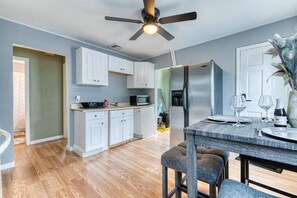 A modern kitchen with white cabinets, a stainless steel refrigerator, and a dining area with a wooden table and bar stools.