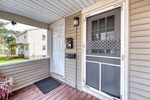 A porch with a wooden deck, a white door, and a screened entry door.