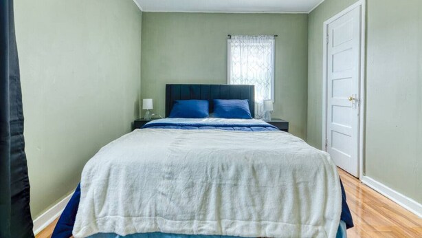 A bedroom with a bed, a nightstand, a window with a curtain, and a door.