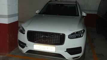 A white car parked in a dimly lit parking garage with concrete walls and a metal staircase.