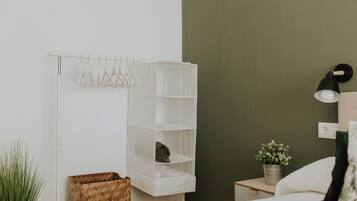 A neatly organized bedroom with a white wardrobe, a bedside table with a lamp, and a potted plant.