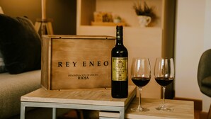 A wooden box labeled "REY ENEO" with a bottle of wine and two glasses on a small table.