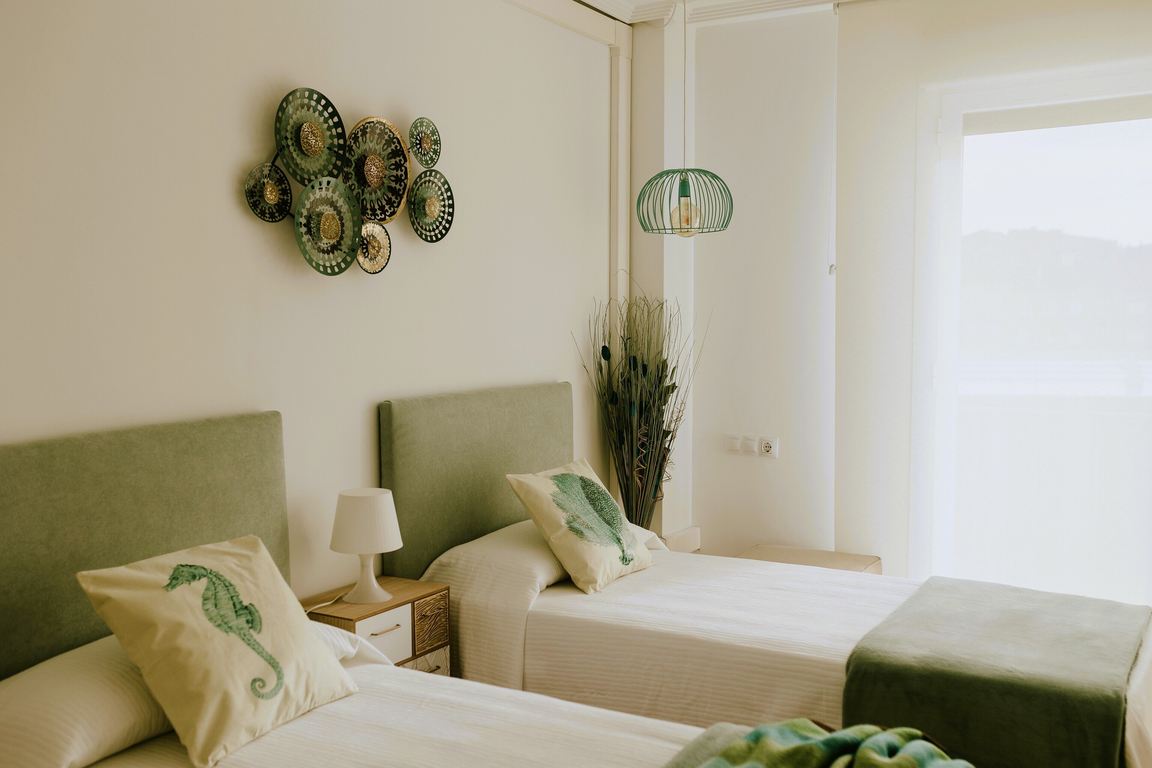 Une chambre d’hôtel avec deux lits, une table de chevet avec une lampe, des œuvres d’art décoratives au mur et une vue sur l’extérieur.
