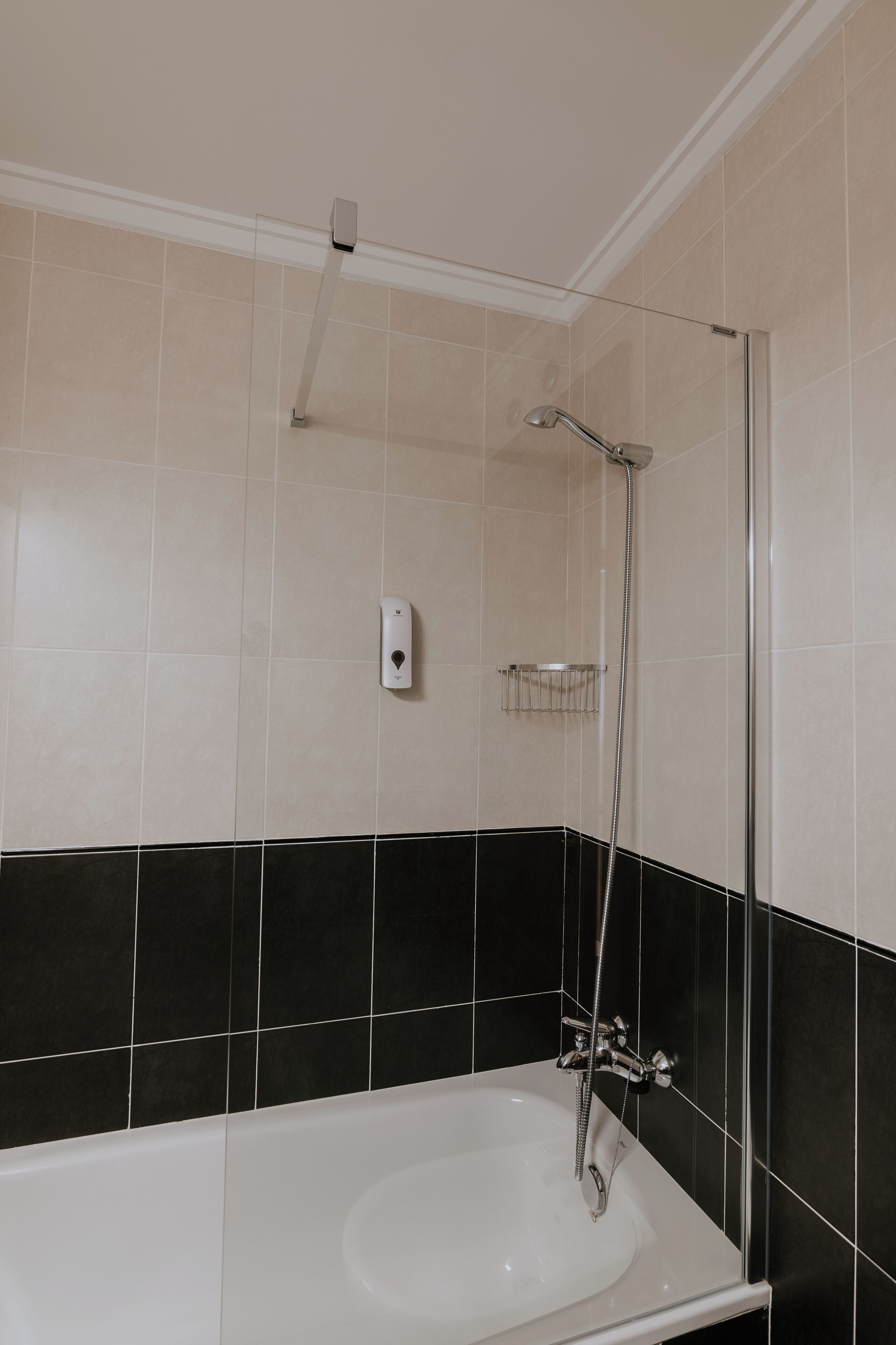 A bathroom with a bathtub, a shower, and a hand dryer on the wall.