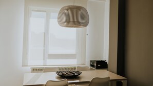 A dining area with a table, chairs, a hanging light fixture, and a window with blinds.