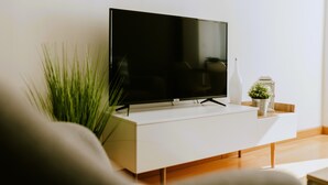 A modern living room with a flat-screen TV on a white console, a potted plant, and a decorative lantern.