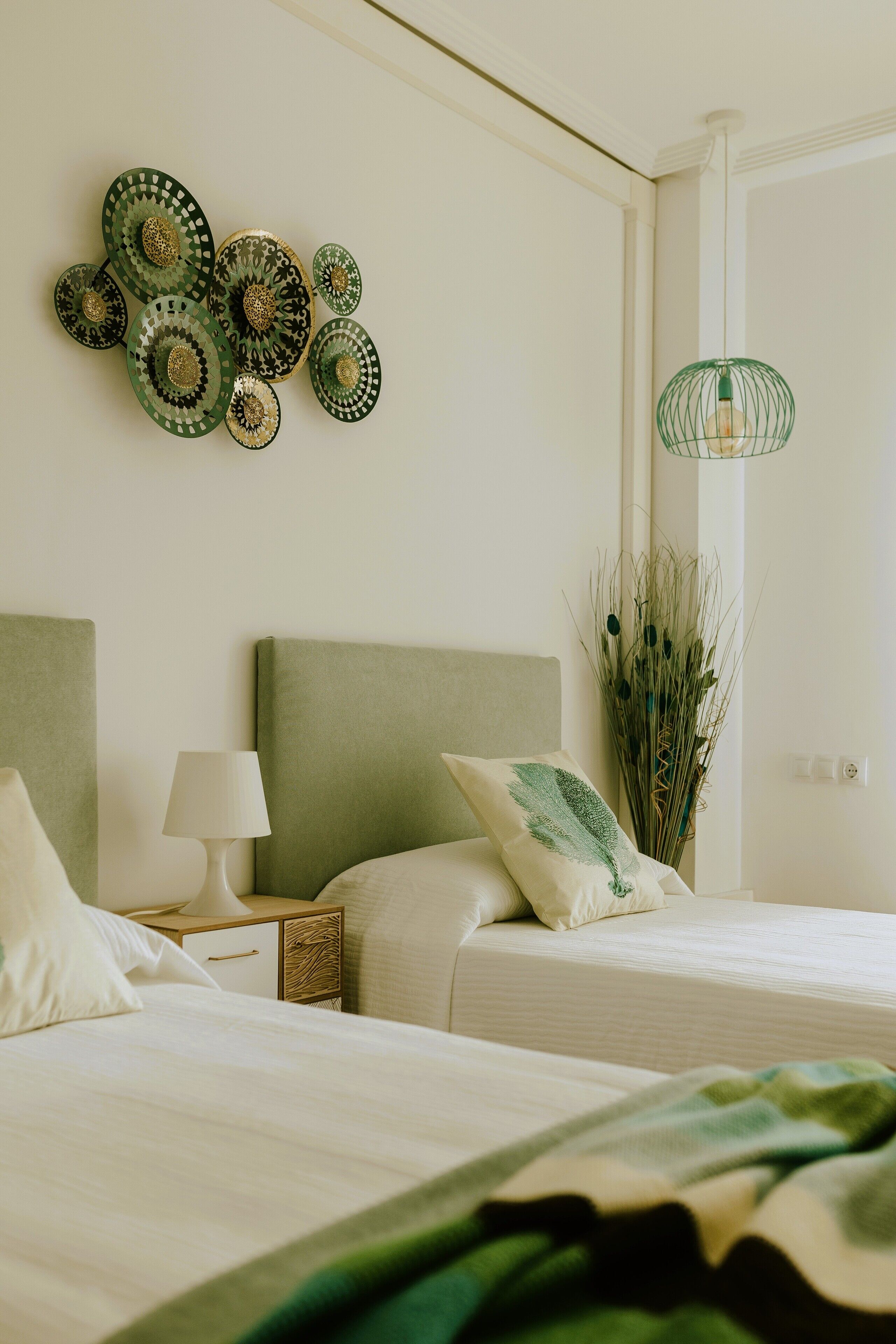 Une chambre avec deux lits, une tête de lit verte, une table de chevet avec une lampe et un élément décoratif mural.