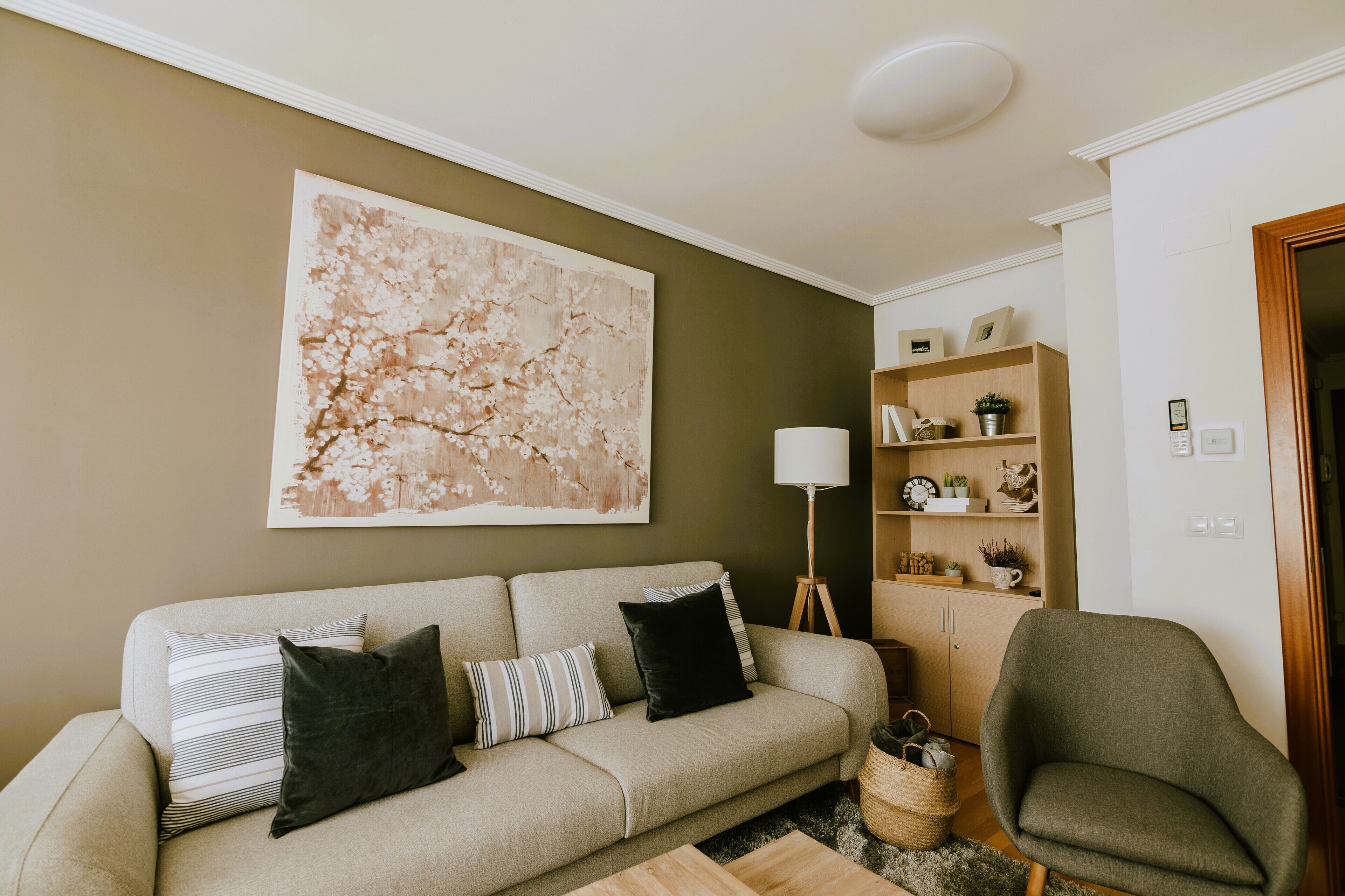 Ett vardagsrum med en beige soffa, en grön fåtölj, en golvlampa och en stor, abstrakt tavla på väggen.