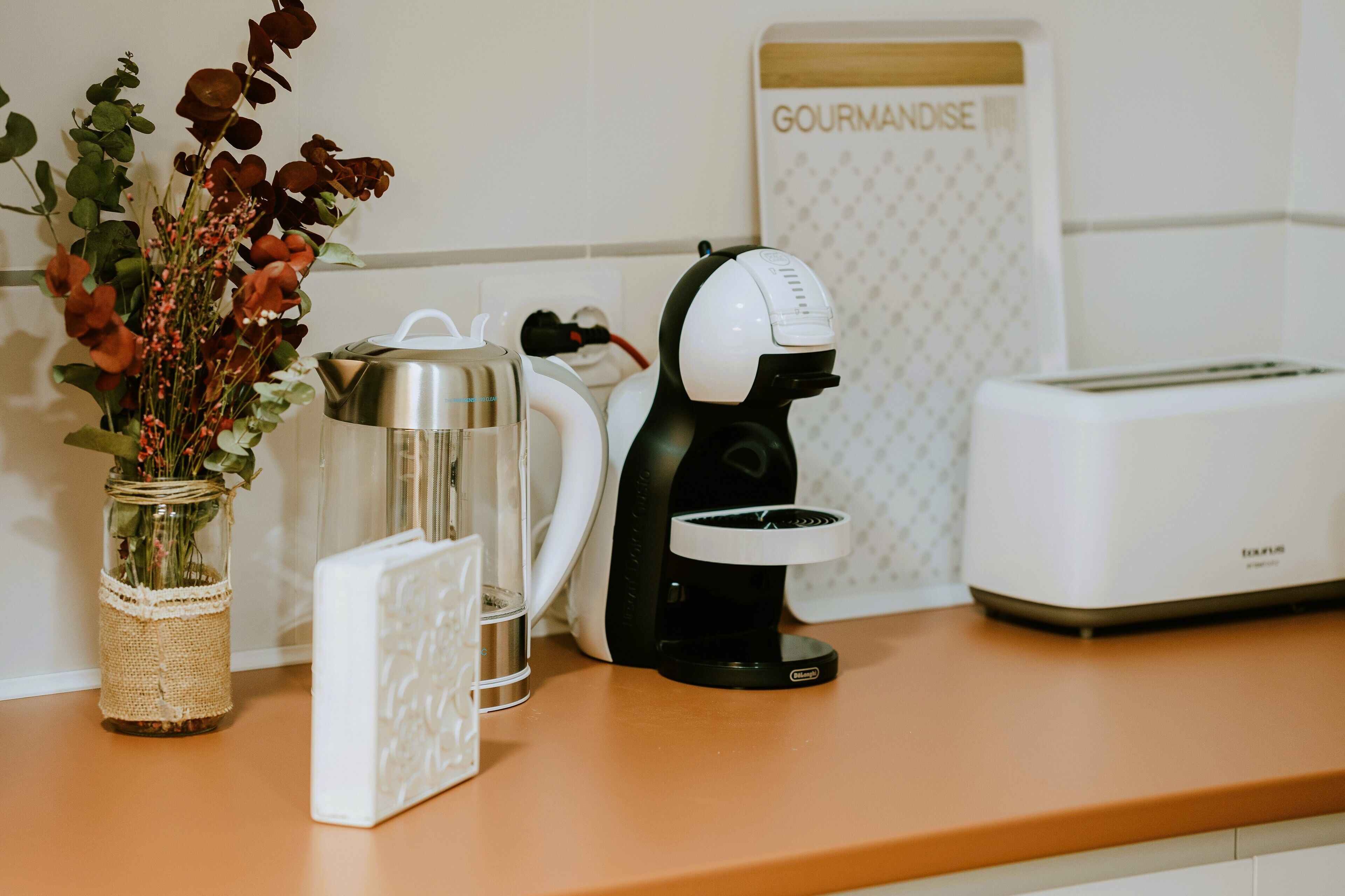 A kitchen counter with a coffee maker, a toaster, and a decorative vase with flowers.