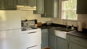 A kitchen with green cabinets, a white stove, and a window with blinds.