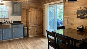 A wooden interior with a kitchen, dining area, and sliding glass door to a backyard.