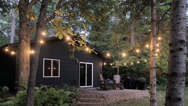 A black cabin with a patio, surrounded by trees and string lights.