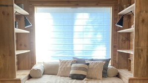 A cozy wooden cabin-style bedroom with a built-in bed, wooden shelves, and a window with blinds.