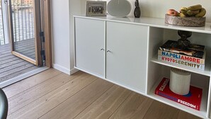 Et moderne værelse med trægulv, et hvidt skab, et dekorativt spejl, en lampe og udsigt udendørs gennem en glasdør.